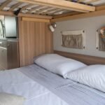 Interior de una furgoneta camper equipada para dormir colchon, ropa de cama suave y vistas panorámicas